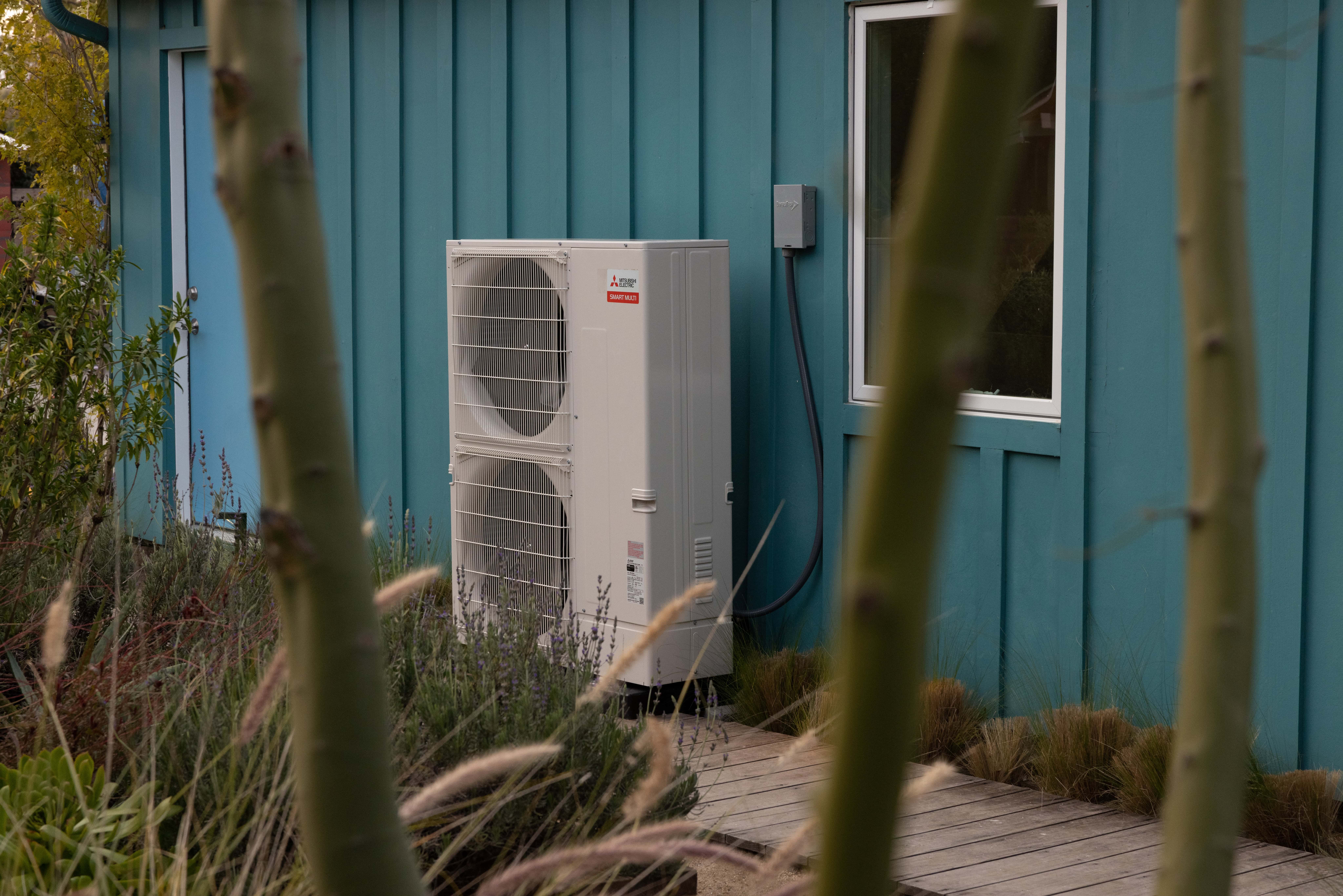 Mitsubishi outdoor heat pump condenser unit beside building