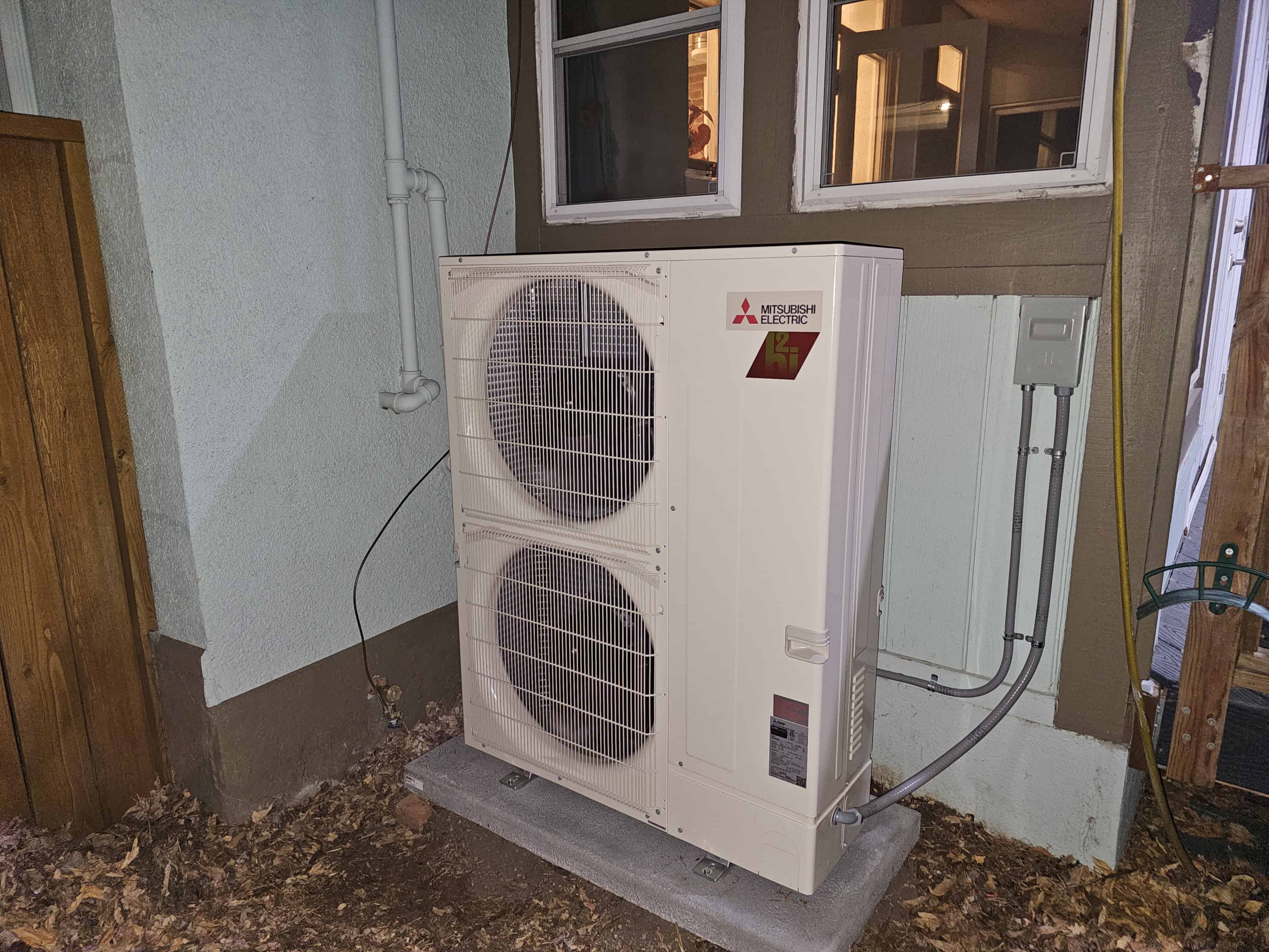 Mitsubishi heat pump outdoor unit on a concrete pad beside a home