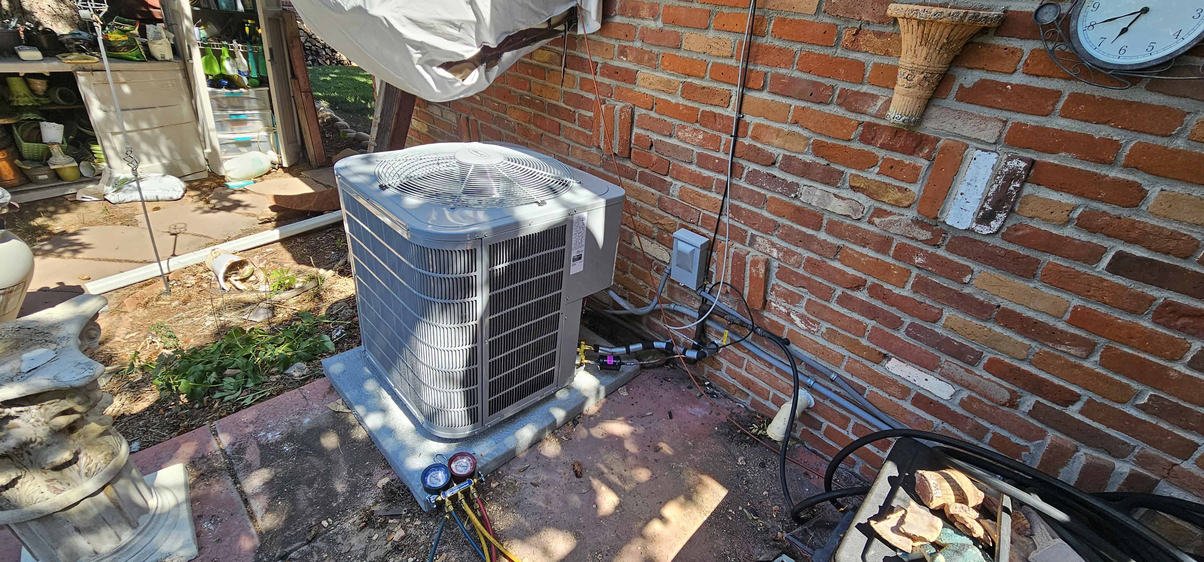 Older white air conditioner condenser on a concrete pad against a brick wall